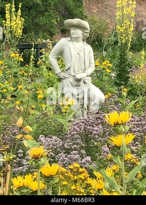 Statue eines kostümierten Mann bei der Arbeit unter Sommer gelb und lila Blüten im Garten im Innenhof bei Delapre Abtei, Northampton Stockfoto