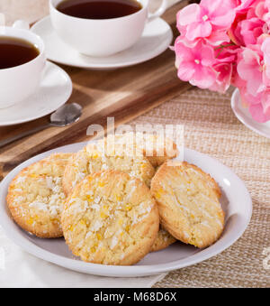 Stapel von Lemon Cookies auf eine Platte mit zwei Tassen Kaffee und Blumen im Hintergrund Stockfoto