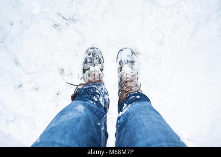 Auf der Suche nach Leder Stiefel im Schnee bedeckt, eine Spitze rückgängig gemacht wird, die goround im abgedeckten im Schnee mit etwas Gras, die Beine haben denim jeans auf Stockfoto