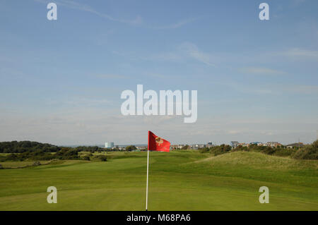 Blick zurück über 1. Grün mit Flagge zu Fahrrinne, Littlehampton Golf Club, Littlehampton, Sussex, England Stockfoto