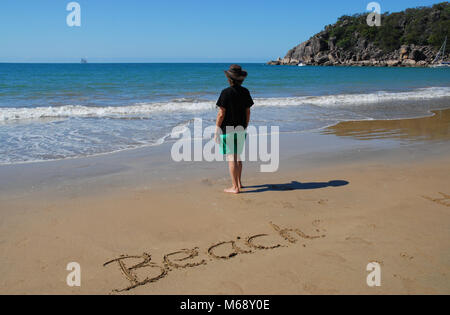 Frau am Strand von Radikalen Bucht hinaus aufs Meer suchen, mit dem Wort Strand in den Sand geschrieben. Magnetic Island, QLD, Australien Stockfoto