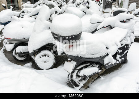Schnee bedeckt zwei- und dreirädrigen Scooter mit geparkt Top Cases draußen in den Straßen von Paris an einem Wintertag. Stockfoto