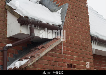 Leichte Erwärmung von Haus Dach und schmelzende Schnee und Eiszapfen Anhäufung in gefrorenen Dachrinnen und mögliche Eindringen von Wasser in die Wände Stockfoto