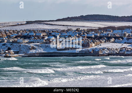 Küste von Moray in Schottland CULLEN BAY GROSSE WELLEN AUF DEM MEER UND IM WINTER SCHNEE AUF DEN HAFEN UND DIE HÄUSER IN DER STADT Stockfoto