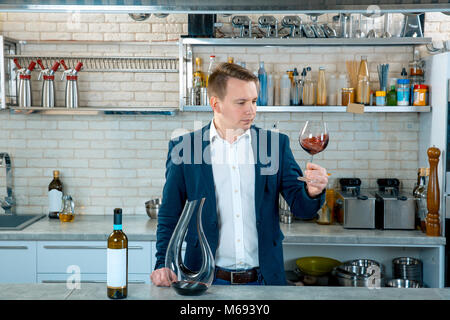 Konzentrierte junge Mann sommelier Verkostung und Rotwein in Glas auf Küche Innenraum Stockfoto