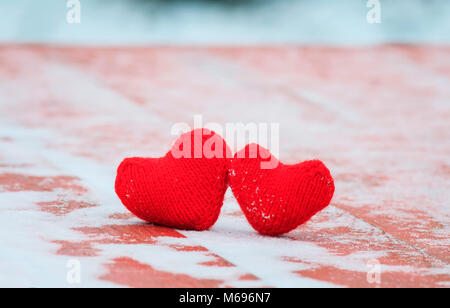 Das Symbol der Liebe zwei rote warmen gestrickten Herzen liegen zusammen auf einem hölzernen Tisch unter dem Schnee Stockfoto