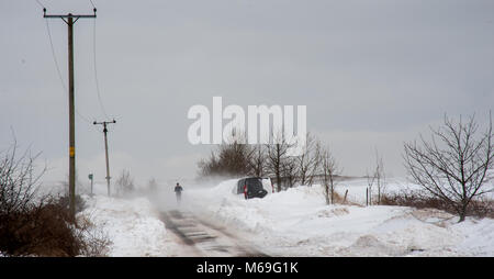 Fernen Mann in Richtung Kamera, die durch schwere Schneeverfrachtung und hinter einem verlassenen van am 24. März 2013 in der Nähe von Bolton, Manchester Stockfoto