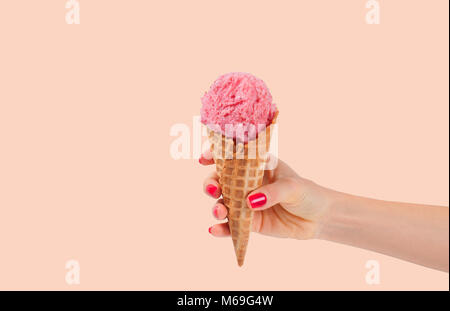 Hand mit Erdbeereis Kegel auf verblasste pastellfarbenen Hintergrund. Erdbeereis in der Wafer Cup. Stockfoto