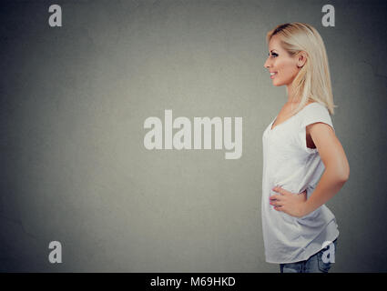 Seitenansicht der beiläufigen Blondine mittleren Alters steht selbstbewusst mit den Händen auf der Taille weg schauen. Stockfoto