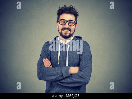 Junge hipster Mann mit Bart, Brille und lächelnd an der Kamera stehend mit Hände gekreuzt. Stockfoto