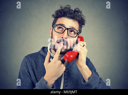 Junge legerer Mann in Verwirrung beim Gespräch am Telefon vor grauem Hintergrund. Stockfoto