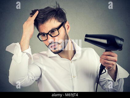 Jungen gutaussehenden Mann in weißem T-Shirt und Brillen Pflege Haar mit Haartrockner, zuversichtlich. Stockfoto