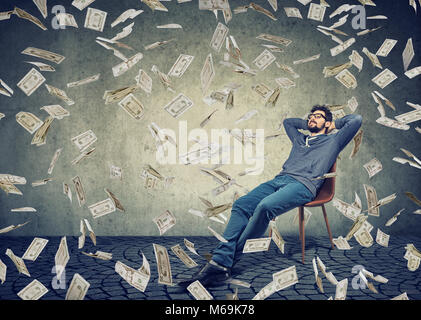 Junge Inhalt Mann sitzt auf Stuhl in Regen Der fliegende Wechsel Inhalte mit der finanziellen Unabhängigkeit. Stockfoto
