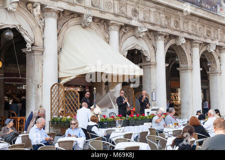 Musiker spielen klassische Musik außerhalb des Caffe Chioggia an der Piazza San Marco, Venedig, Italien als Touristen sitzen an den Tischen genießen Sie den Herbst Sonnen