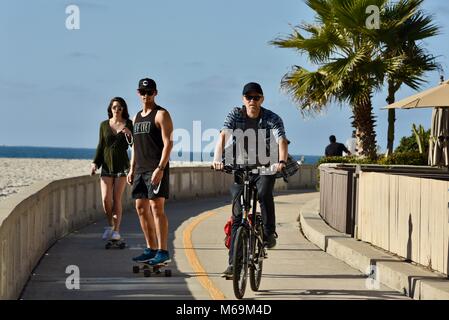 Man Radfahren und junges Paar skateboarding am beliebten Strand gepflasterten Promenade in Mission Beach, San Diego, Kalifornien, USA Stockfoto