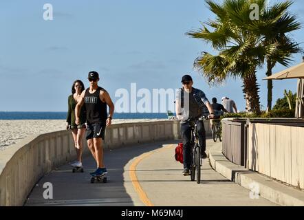 Man Radfahren und junges Paar skateboarding am beliebten Strand gepflasterten Promenade in Mission Beach, San Diego, Kalifornien, USA Stockfoto