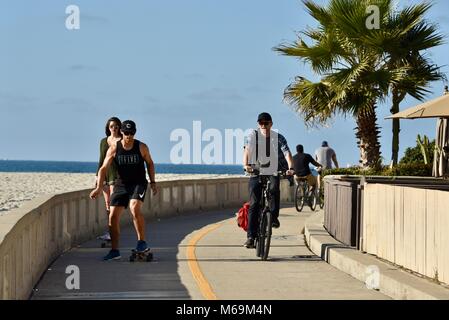 Man Radfahren und junges Paar skateboarding am beliebten Strand gepflasterten Promenade in Mission Beach, San Diego, Kalifornien, USA Stockfoto