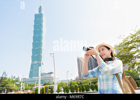 Junge positive weibliche Asiatische backpacker Foto bei den Park vor der Taipei 101. Konzentrieren Sie sich auf Ihre Kamera. Travel Concept. Auf der Seite. Stockfoto