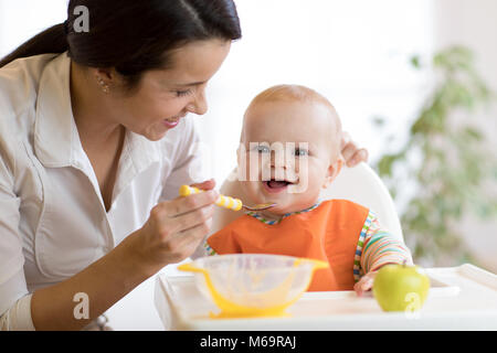 Mom, Homogenisierten auf ihr Baby Sohn auf hohen Stuhl in der Küche. Stockfoto