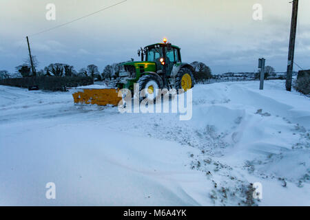 Ein Traktor mit einem Schnee auf den Pflug vorn montiert das Pflügen der Hauptstraße in einer abgeschnittenen Dorf wegen Sturm Emman und das Tier aus dem Osten im Lixwm, Flintshire, Wales, Vereinigtes Königreich Stockfoto