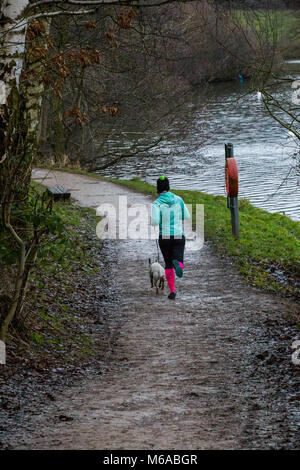 Eine Dame tragen brithgly Farbige lycra Jogging im Park mit ihren Hund im Winter und das Tragen eines Bobble hat Stockfoto