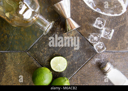 Zutaten für Margarita Cocktail mit Alkohol Flasche, Limes, Salz und Eiswürfel mit Salz umrandet Glas auf Granit. Stockfoto