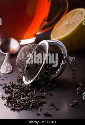 Teesieb mit einer Tasse Tee auf einem dunklen Hintergrund. Stockfoto