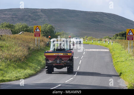 Ansicht der Rückseite des Tractor Pulling Düngerstreuer & vorne Mercedes Cabrio fahren & Reisen auf Landstraße - North Yorkshire, England, UK. Stockfoto