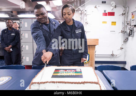 Pazifik (Feb. 25, 2018) Senior Chief Gas Turbine Systems Techniker Claude Marcelin (links), von Miami und Seaman Jalicia Jäger (rechts), von Mobile, Ala., schneiden Sie einen Kuchen Feiern Afroamerikaner/Monat Geschichte auf das Chaos Deck der Arleigh-Burke-Klasse geführte Anti-raketen-Zerstörer USS Dewey (DDG105) als die Älteste und jüngste Crew Mitglieder der afrikanischen amerikanischen Abstieg. Diese Tradition symbolisiert das Vermächtnis der afrikanischen amerikanischen Matrosen in der Geschichte der Navy. Dewey ist in den Indopazifischen region Interoperabilität mit Partnern zu verbessern und dienen als eine fertige Antwort für Stockfoto