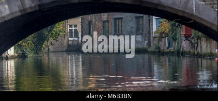 Ein Blick durch ein Brügge Brücke, wo die Gebäude im ruhigen Wasser des langen Wasserwege canal System widerspiegeln. Stockfoto