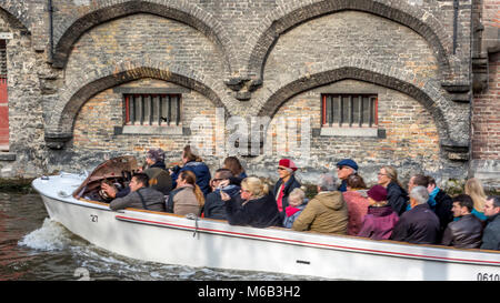 Tour Boot voller Touristen auf dem Kanal in Brügge vorbei an alten Ziegel filigrane Bögen. Stockfoto