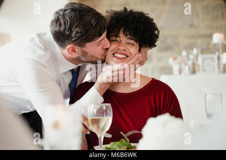Hochzeit Gäste Spaß am Essen. Eine Frau mit einem afro erhält einen dicken Kuss auf die Wange von der Bräutigam zu seiner Hochzeit. Stockfoto