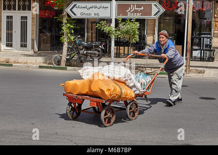 Kashan, Iran - 27. April 2017: Ein alter Mann schiebt einen handkarren vor ihm auf der Fahrbahn einer Strasse der Stadt. Stockfoto