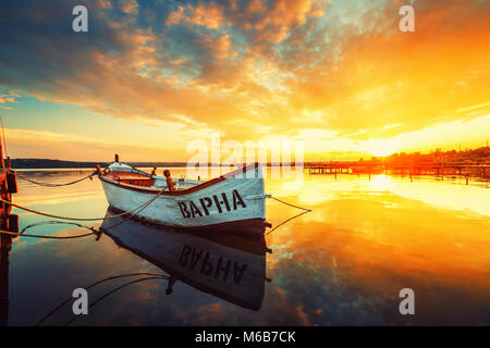 Fischerboot auf Varna See mit einem Spiegelbild im Wasser bei Sonnenuntergang. Stockfoto