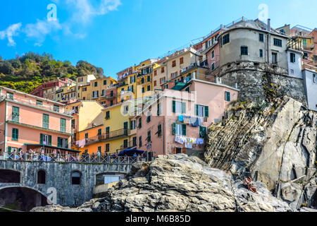 Die felsige Küstenlinie von Manarola Italien, Teil der Cinque Terre an der ligurischen Küste der italienischen Riviera mit Hang Häuser und ein Paar auf Felsen Stockfoto