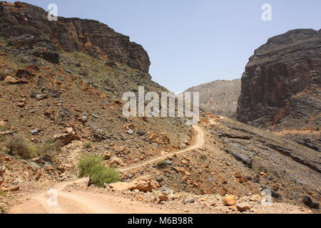 Einsame Schotterstraße durch eine karge Landschaft von dunklen Felsen im Oman. Stockfoto
