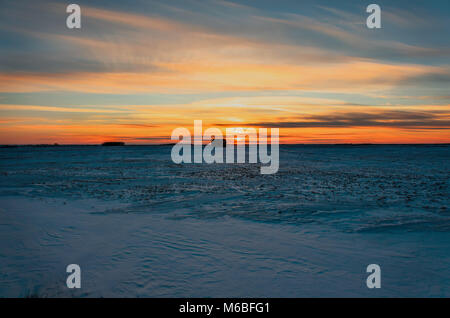 Riesige blaue Himmel in rosa Wolken bei Sonnenuntergang der Tag, eine orange rot Glühen von der Sonne über einem schneebedeckten Feld mit einem schwarzen Silhouette einer Hütte und einem gr Stockfoto