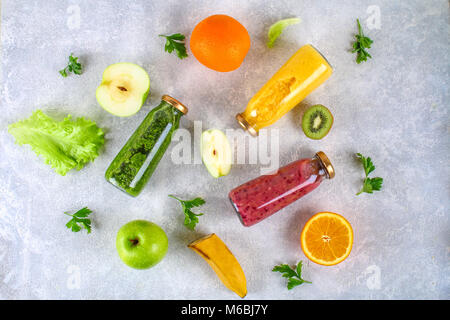 Grün, Gelb, Violett Smoothies im johannisbeere Flaschen, Petersilie, Apfel, Kiwi, Orange auf einem grauen Tabelle. Flach, Ansicht von oben Stockfoto