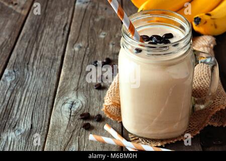 Kaffee, Bananen Smoothie in einem Marmeladenglas. Seitenansicht mit Kopie Raum über eine rustikale Holz Hintergrund. Stockfoto