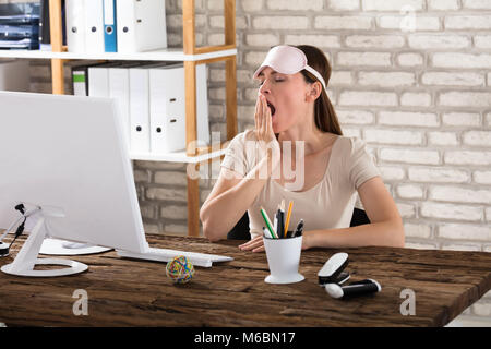 Junge Frau sitzt am Schreibtisch Gähnen im Büro Stockfoto