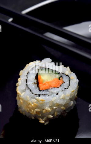 Sushi auf einem schwarzen Schild: Uramaki (Rolle mit Reis auf der Außenseite) und Essstäbchen Stockfoto