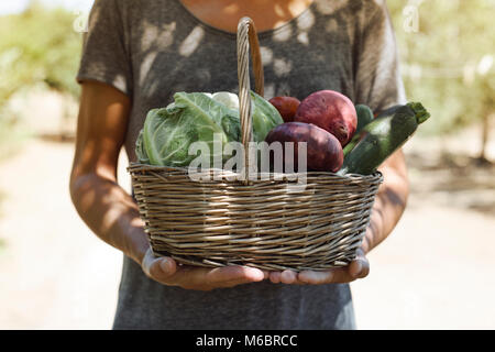 Closeup von einem kaukasischen Jüngling mit einem rustikalen Korb voll mit Gemüse frisch gesammelt in einem Bio-Obstgarten Stockfoto