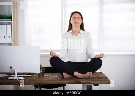 Junge Geschäftsfrau sitzen auf hölzernen Schreibtisch Meditieren im Büro Stockfoto