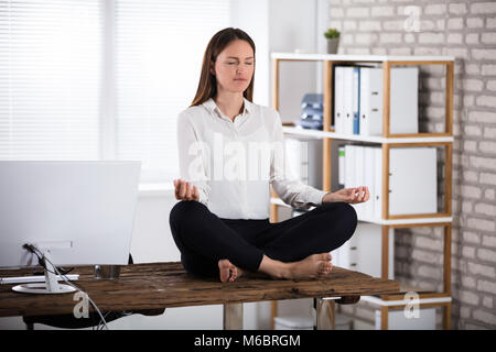 Junge Geschäftsfrau sitzen auf hölzernen Schreibtisch Meditieren im Büro Stockfoto
