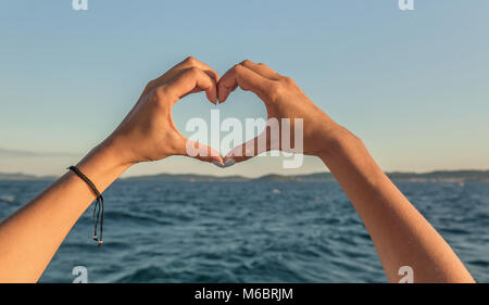 Hände in der Form von Herzen vor dem Hintergrund des Meeres. Stockfoto