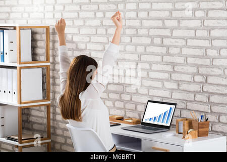 Erfolgreiche Geschäftsfrau Sitzen auf Stuhl heben ihre Hände mit Graph auf dem Laptop Bildschirm Stockfoto