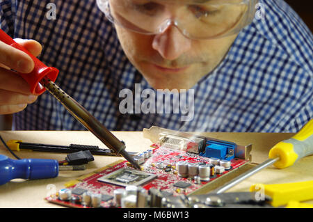 Techniker konzentrierte sich auf die Reparatur von elektronischen Geräten. Ein Mann bei der Arbeit mit einem Lötkolben. Stockfoto