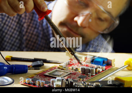 Ein Mann bei der Arbeit mit einem Lötkolben. Techniker konzentrierte sich auf die Reparatur von elektronischen Geräten. Stockfoto