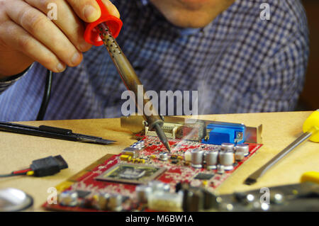 Ein Mann bei der Arbeit mit einem Lötkolben. Techniker konzentrierte sich auf die Reparatur von elektronischen Geräten. Stockfoto