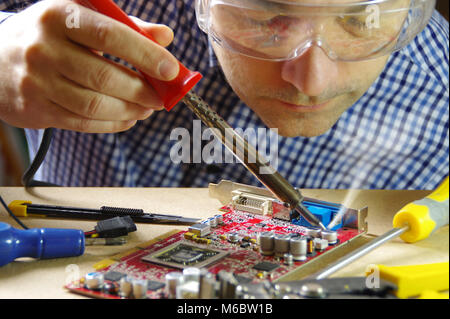 Ein Mann bei der Arbeit mit einem Lötkolben. Techniker konzentrierte sich auf die Reparatur von elektronischen Geräten. Stockfoto